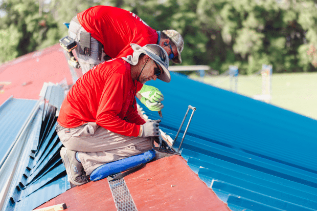 A picture of two Big D team members wearing red shirts securing metal roofing on top of a commercial building.