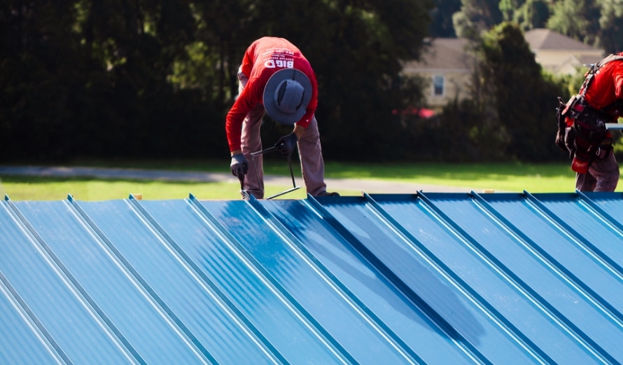 Picture of a Big D Employee installing a blue metal roof on a commercial building.