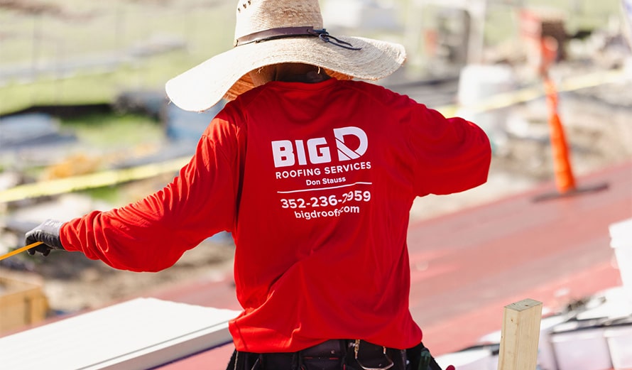 Picture is of a Big D team member with a red Big D shirt working on top of a commercial roof.