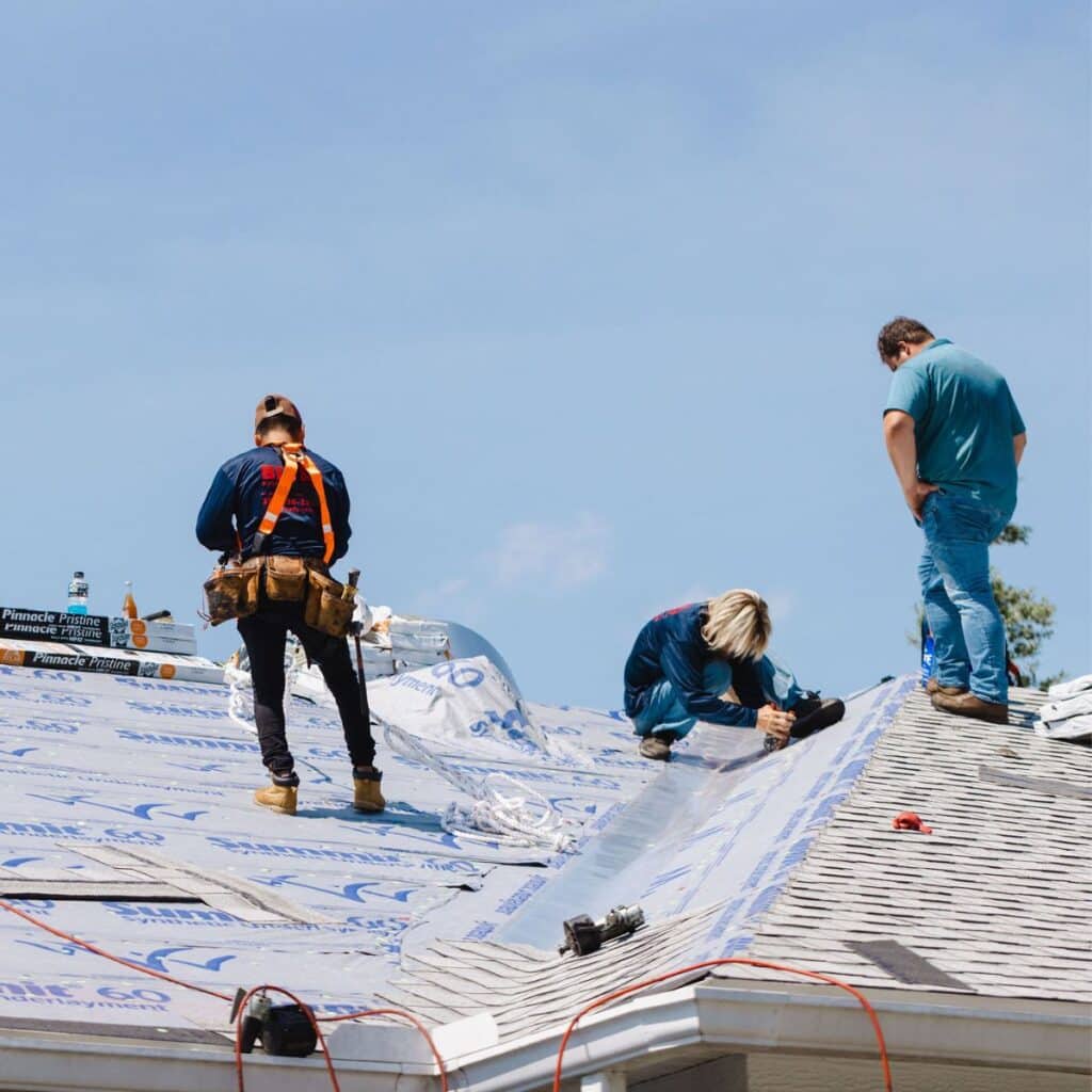 An image of 3 men laying underlayment and asphalt shingles over the roof deck.